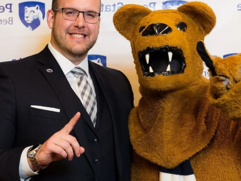 A person stands with the Nittany Lion, both hold up their index fingers